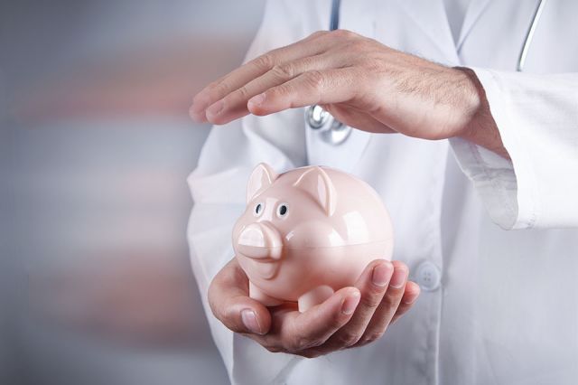 Foto: Arzt hält Hand über Sparschwein